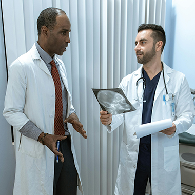 two doctors in white coats talking while holding an xray