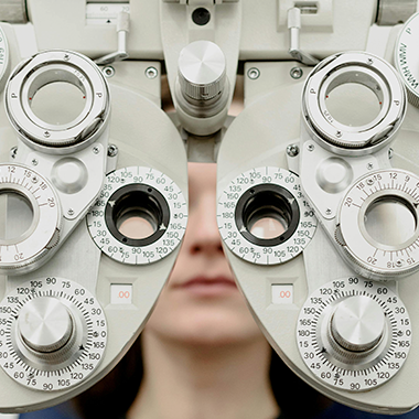 Patient in a chair testing their eye sight through a Phoropter